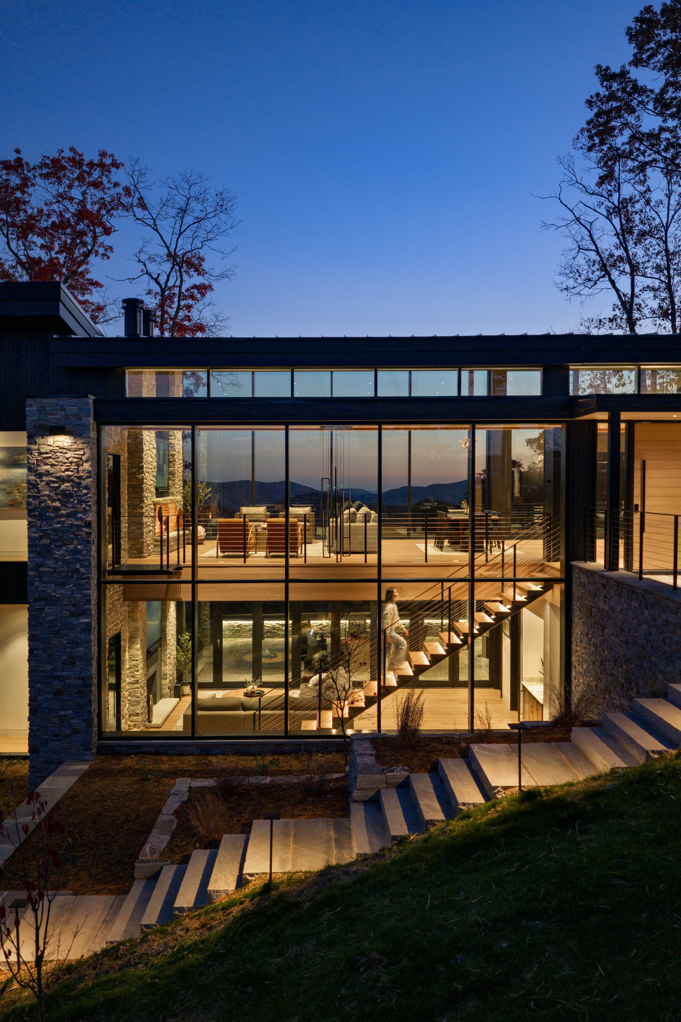 Mountain home at dusk with stone, steel, and full-height glass